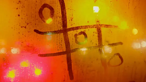 Tris game written in the bus window with finger in misted glass, yellow and red backlight