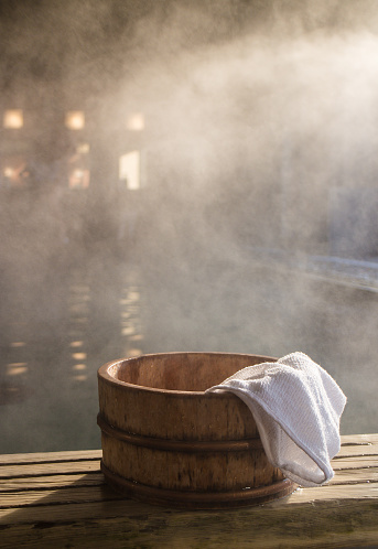 Bath bucket with a towel at blurred and fogged hot spring bath at Japanese onsen. Shot in the light of rising sun.