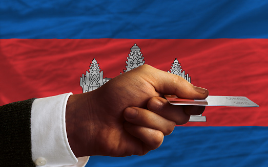 man stretching out credit card to buy goods in front of complete wavy national flag of cambodia