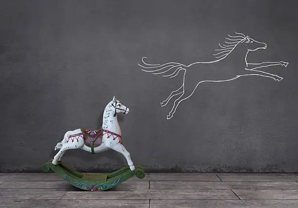 Side view of wooden rocking horse on wooden floor with running (or jumping) horse sketched (chalk drawing) on the wall.