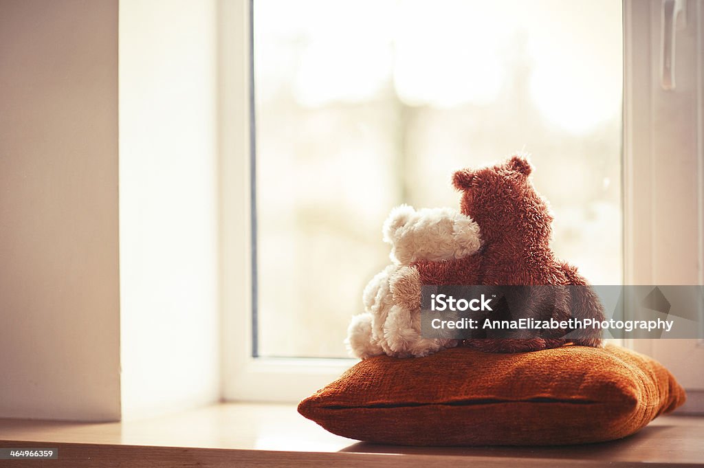 Two embracing teddy bear toys sitting on window-sill Two embracing teddy bears looking through the window sitting on window-sill. Teddy Bear Stock Photo