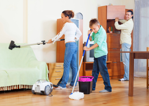 Ordinary family of three with teenager doing housework with  cleaning equipment in living room