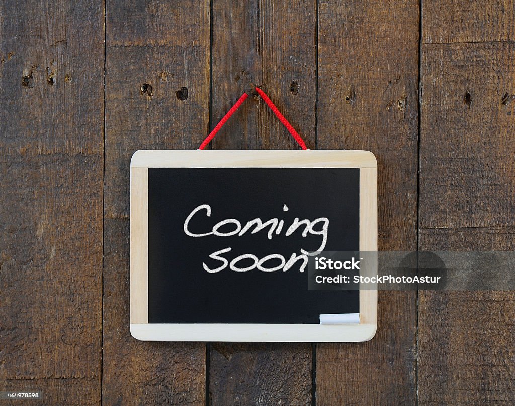 Coming soon sign nailed to a wooden wall Blackboard hanging on a old wooden wall with phrase Coming soon. Opening Stock Photo