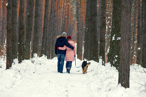 Young couple in love with dog walking in the snowy forest back to camera