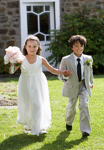 Portrait Of Bridesmaid With Page Boy Portrait Of Bridesmaid With Page Boy Walking Towards Camera Smiling flower girl stock pictures, royalty-free photos & images