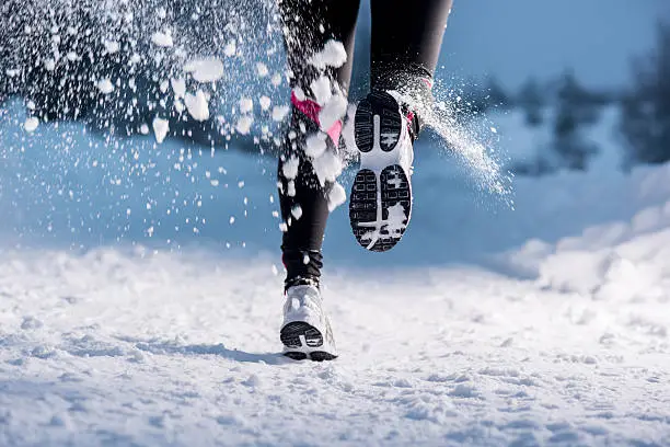 Athlete woman is running during winter training outside in cold snow weather.