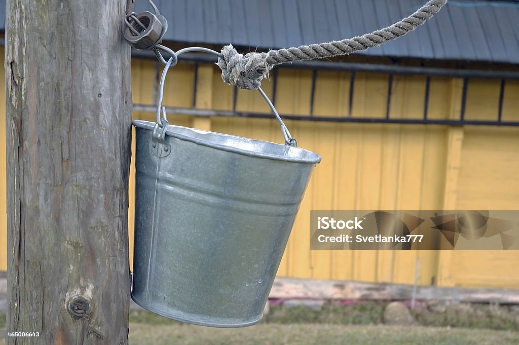 Bucket. Bucket of a well hanging on a rope and a hook against the wall of a house. Alternative Lifestyle Stock Photo