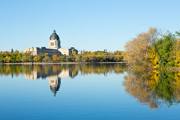 The Saskatchewan Legislative Building is reflected in Wascana Lake on a beautiful, sunny autumn morning in Regina, Saskatchewan, Canada.