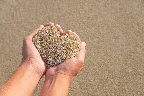manos sosteniendo una playa en forma de corazón - sandy brown fotos fotografías e imágenes de stock