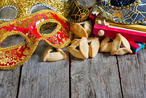 Hamantaschen cookies or Haman's ears, noisemaker and carnival masks for Purim celebration (jewish holiday). Copy space background.
