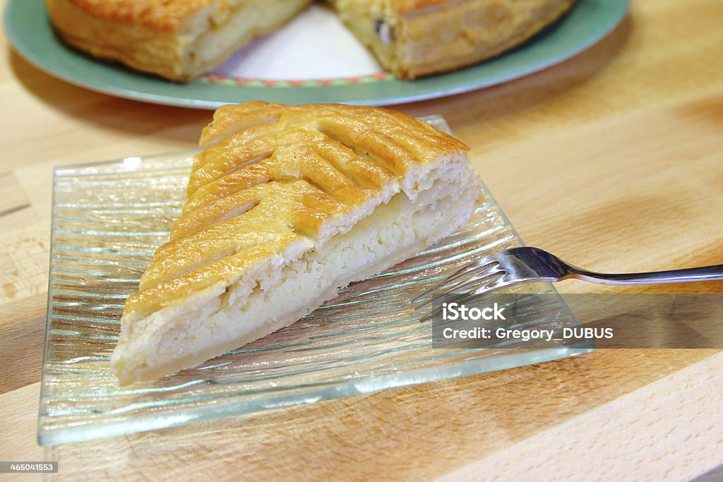 Epiphany cake ready to eat Epiphany cake (also called king's cake) with frangipane, selective focus. A porcelain bean is hidden inside the cake. Wood background. Almond Stock Photo