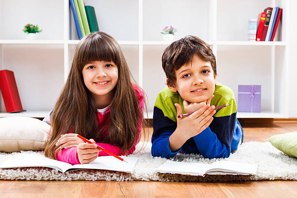 istock Smiling children relaxing on plush carpeting doing homework 465044088