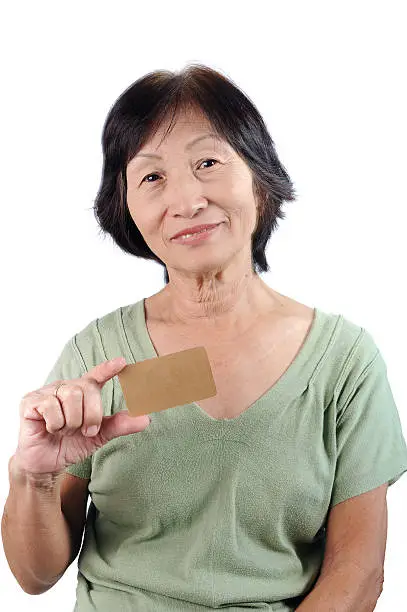 Smiling asian seniorwoman holding blank empty business card isolated in white background