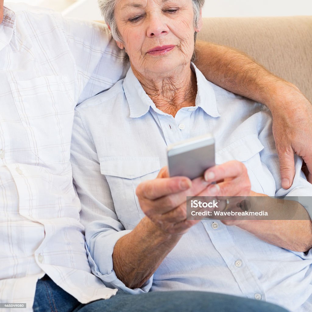 Woman reading text message on smartphone Senior woman reading text message on smartphone while sitting with man at home 2015 Stock Photo