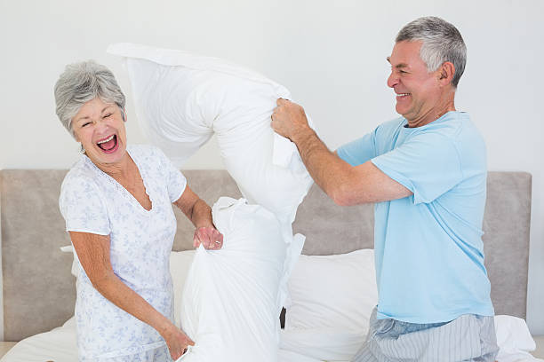 senior par tener lucha con almohada en la cama - bed couple pillow fight men fotografías e imágenes de stock