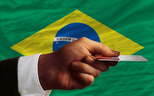 man stretching out credit card to buy goods in front of complete wavy national flag of brazil