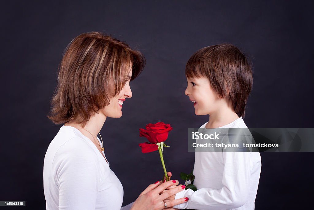 Young kid giving gorgeous red rose to his mom Young kid giving gorgeous red rose to his mom, studio shot isolated on black background Boys Stock Photo