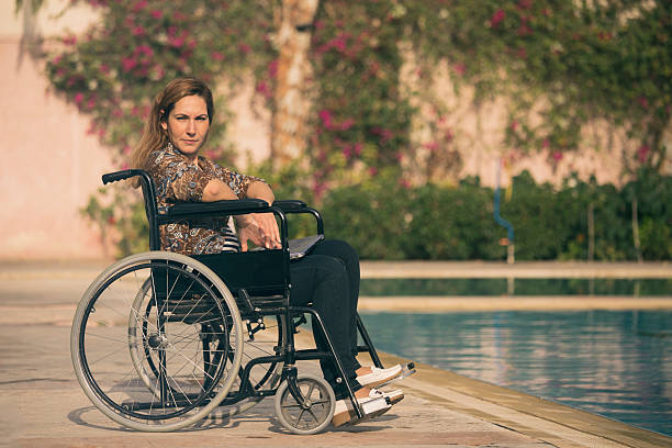 Sea hotel lifeguard assisting a woman with a disability to use accessible services and facilities, a pool chair lift, and a wheelchair, at the resort.