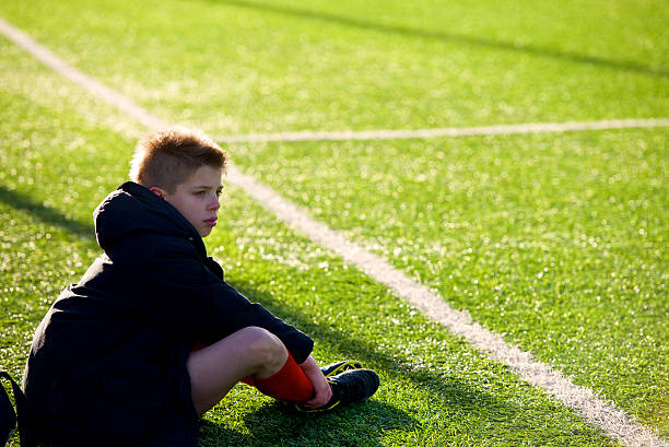 petit joueur de football expulsé triste assis sur les limites du terrain - soccer guilt soccer player sitting photos et images de collection