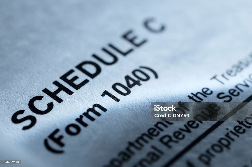 Close up of Schedule C from 1040 Tax Form A close up from the Schedule C of the 1040 Tax form.  A beam of light rakes across the document.  It is photographed with a very shallow depth of field and a cool blue is the dominate color scheme.  Schedule C is the tax form on which U.S. small businesses and sole proprietors report their income. Self-Employment Stock Photo