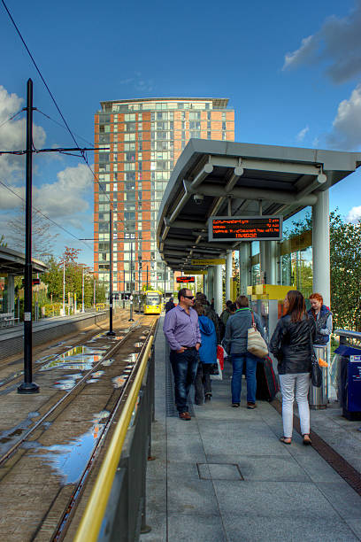 Manchester, United Kingdom - October 4, 2014: The Media City station in Salford Quays with a Metrolink Tram approaching the platform and tourists and commuters waiting on the platform.