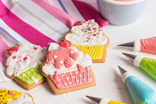 Colorful icing cookies in cupcake shape on white background and cornets with glaze for painting