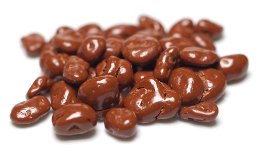 heap of chocolate covered cranberries or raisins on a white background. Shallow depth of field