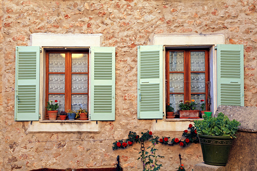 Two french rustic windows with old green shutters and flower pots in stone rural house, Provence, France.