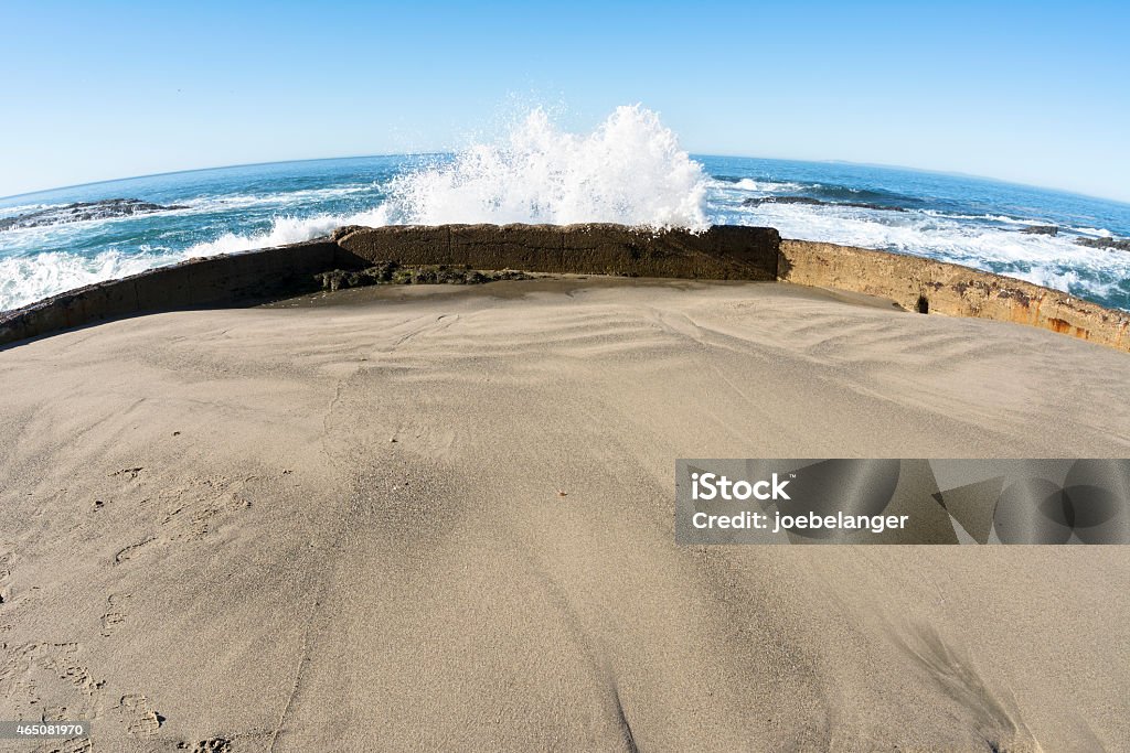 Sea wall blocking wave A sea wall protects a small, enclosed sandy beach from oncoming waves as they crash and splash high into the air. 2015 Stock Photo