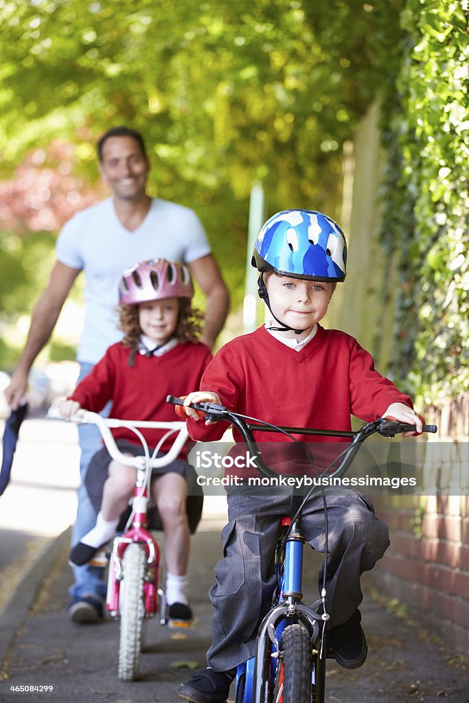 Two children riding bikes with their father White British Children Riding Bikes On Their Way To School With Father Child Stock Photo