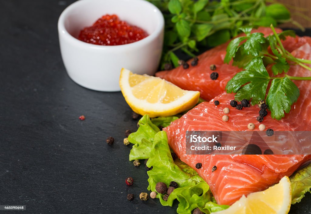 Fresh salmon and red caviar on black plate Fresh salmon with lemon, parsley, pepper and red caviar on black plate Rear View Stock Photo