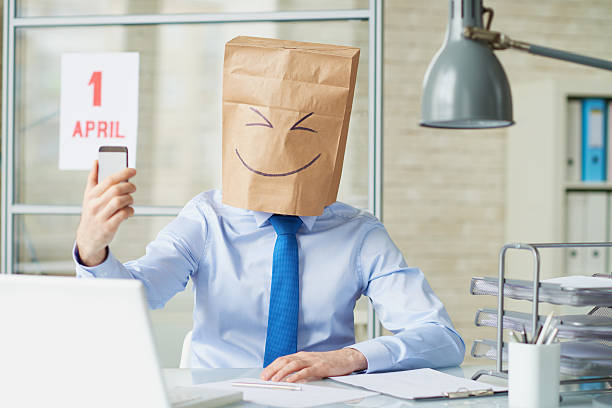 Office worker wearing paper bag taking a selfie with smart phone on April fools day