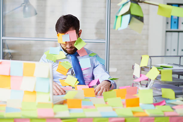 Office worker sitting at table and sleeping, he and his workplace covered with adhesive notes