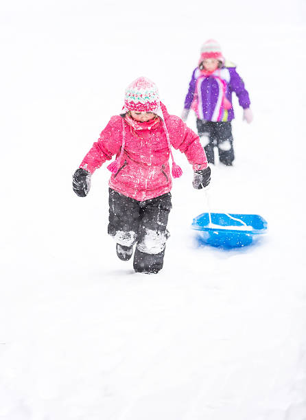 istock Girls Playing in Snowstorm With Sled 465105588