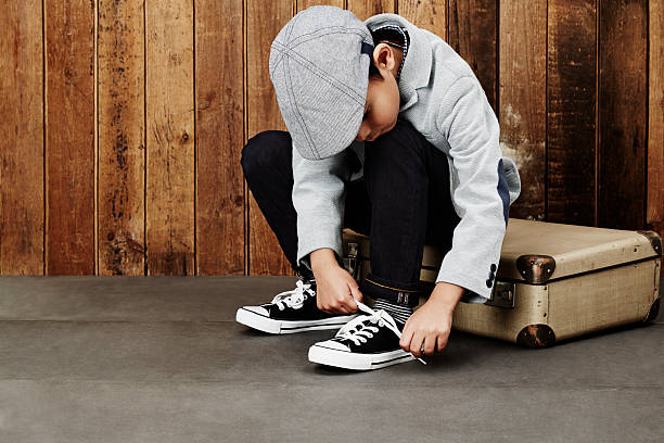 Boy tying shoelace on case Young boy tying shoelace sitting on suitcase flat cap stock pictures, royalty-free photos & images