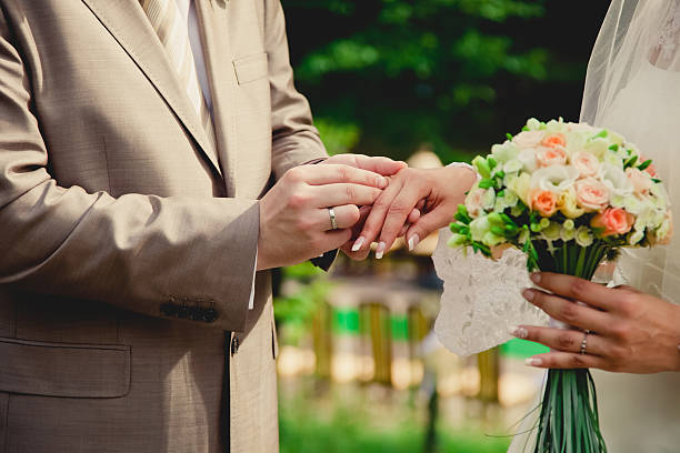 istock mans hand putting a wedding ring on the brides finger 465118436