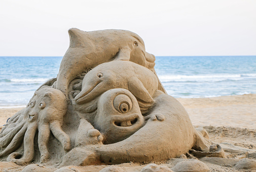 Stock photo showing sandy beach with a sandcastle made with a bucket with a mold shape, in the distant background a boat with punt for tourist cruises is seen, ready for a tour gide to show people around the area