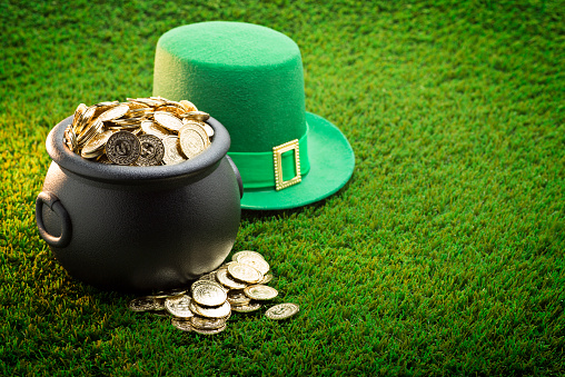 This is a close up photo of a large black pot of gold on the grass with a green hat symbolizing St. Patrick's Day.