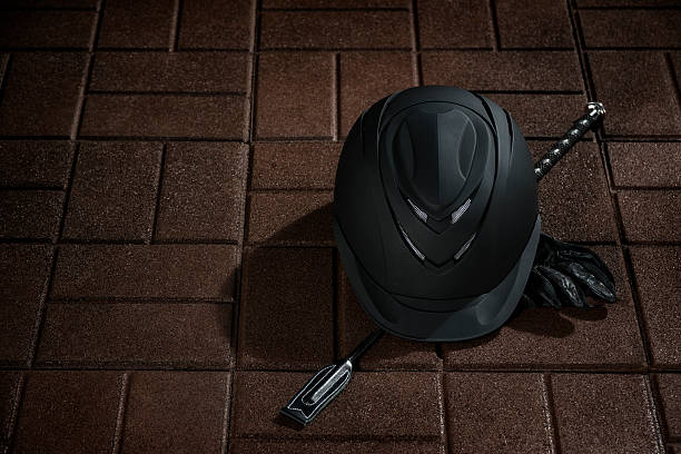 Equestrian riding helmet, crop and gloves sitting on a rubber tile floor of a barn.