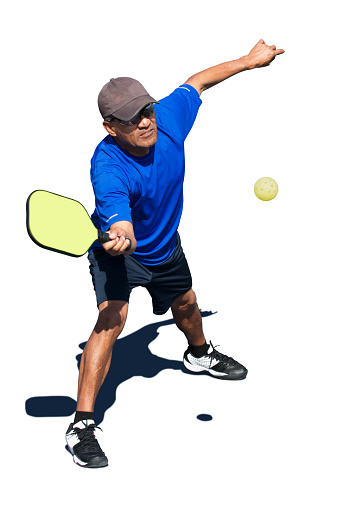 Isolated image of an adult man playing swinging at a pickleball during a pickleball match.  Includes paths for player, ball and shadow