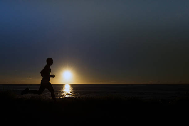 A silhouette of jogger at a grassy path along the ocean.