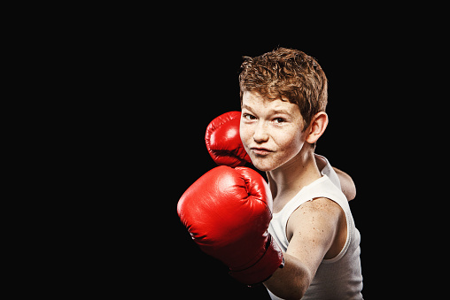 Red-haired boy on a black background with red boxing gloves