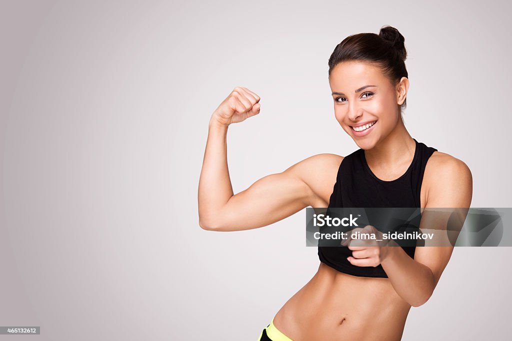 Mixed race woman demonstrating biceps Cheerfully smiling mixed race sporty woman demonstrating biceps, isolated on white background 20-29 Years Stock Photo