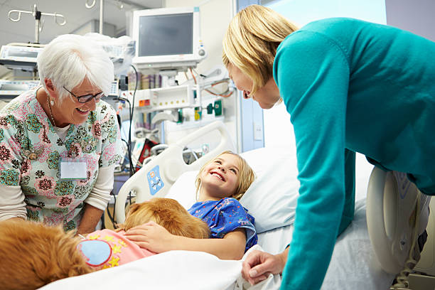 A girl lays in a hospital bed while smiling at two adults Young Girl Being Visited In Hospital By Therapy Dog And Family animal therapy stock pictures, royalty-free photos & images