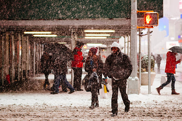 New York City, NY, USA - March 1, 2015: Heavy snow falls in Times Square and people rush to their destination. African American man in puffer coat crosses, followed by a woman in burgundy hat. Don't walk sign. 