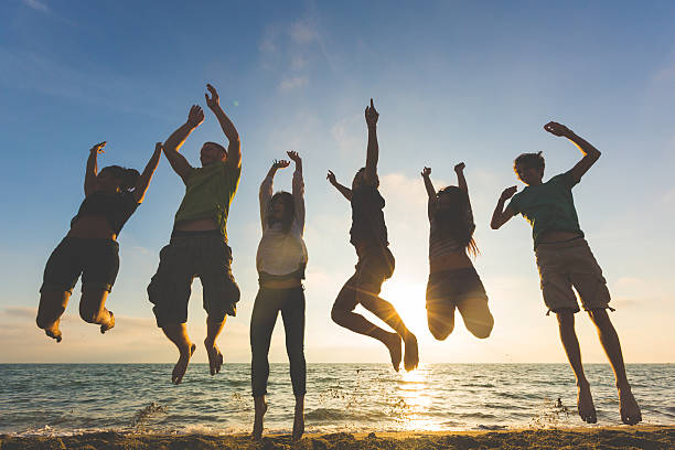 istock Group of people jumping up by the beach at sunset 465138624