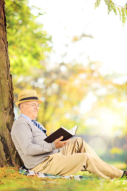 istock Senior man sitting on grass and reading a book 465143703