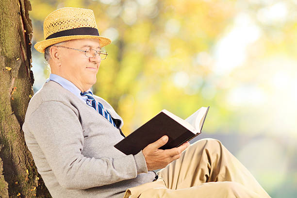 istock Senior man sitting on grass and reading a book 465145823