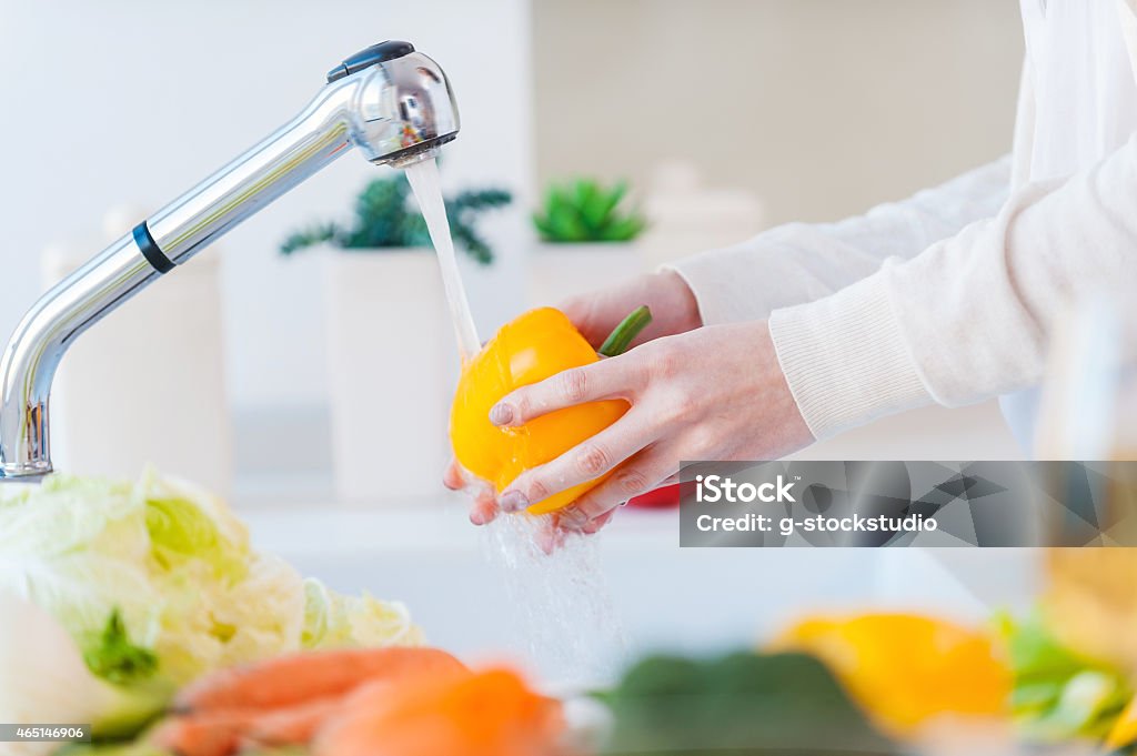 Woman washing vegetables. Beautiful young woman washing vegetables for salad and smiling while standing in the kitchen 2015 Stock Photo