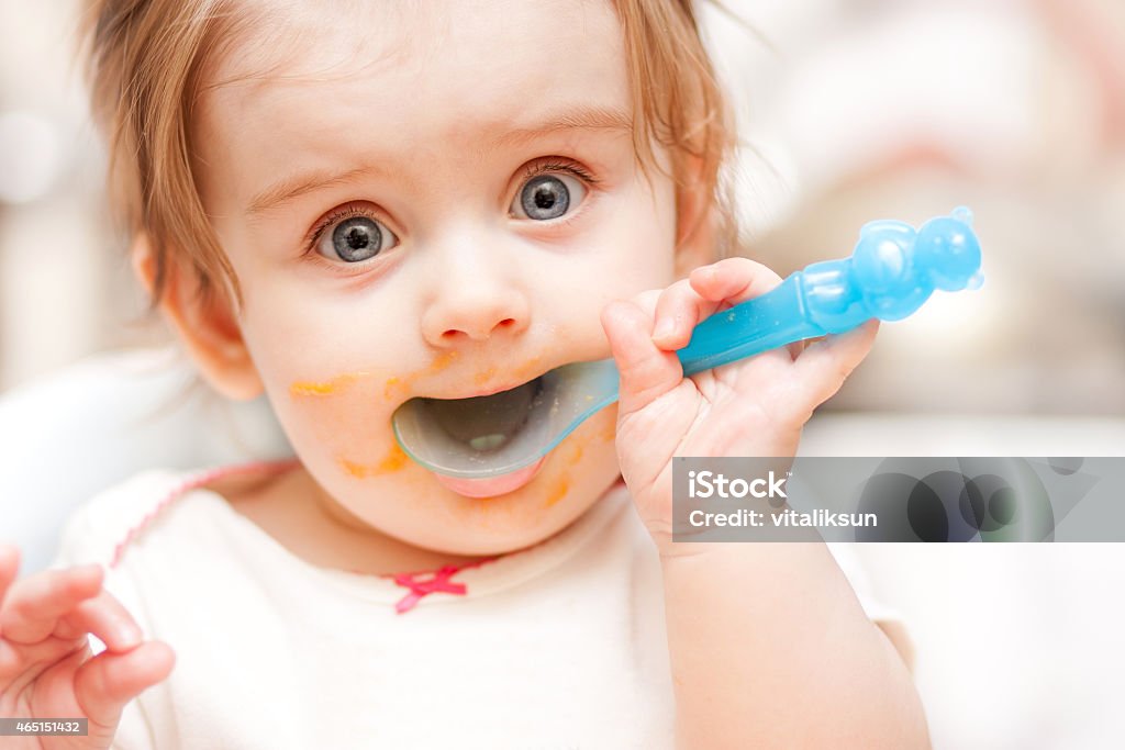 little girl feeding from a spoon on blue chair. little girl feeding from a spoon on blue chair 2015 Stock Photo